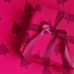Pu&ograve; includere: Un regalo avvolto in carta magenta con un motivo di alberi di Natale magenta scuro. Il regalo &egrave; legato con un nastro e un fiocco magenta. Lo sfondo &egrave; dello stesso colore magenta con il motivo dell'albero di Natale.