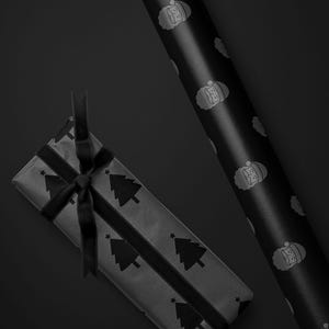 Pode incluir: Um presente embrulhado com uma fita preta e um rolo de papel de embrulho. O papel de embrulho apresenta um padr&atilde;o de &aacute;rvores de Natal e estrelas. O rolo de papel tem um padr&atilde;o de rostos de Papai Noel. O fundo &eacute; preto.
