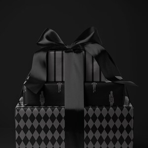 Peut inclure: Une pile de cadeaux emball&eacute;s en noir et gris. La bo&icirc;te cadeau du bas pr&eacute;sente un motif de losanges, la bo&icirc;te du milieu un motif de soldat et la bo&icirc;te du haut des rayures verticales. Un grand n&oelig;ud en satin noir orne le tout.