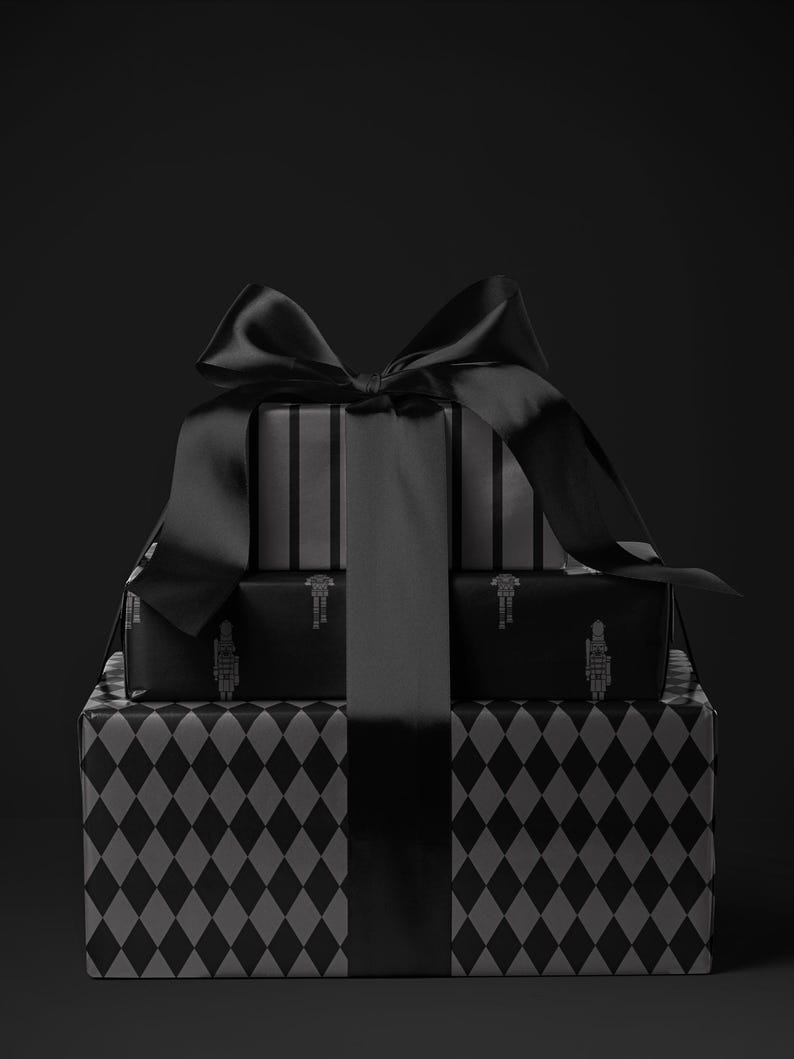 Peut inclure: Une pile de cadeaux emball&eacute;s en noir et gris. La bo&icirc;te cadeau du bas pr&eacute;sente un motif de losanges, la bo&icirc;te du milieu un motif de soldat et la bo&icirc;te du haut des rayures verticales. Un grand n&oelig;ud en satin noir orne le tout.
