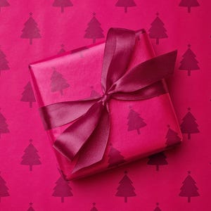 Pu&ograve; includere: Un pacco regalo avvolto su uno sfondo magenta. La carta da regalo e lo sfondo presentano un motivo ripetuto di alberi di Natale magenta scuro. Un nastro magenta scuro &egrave; legato attorno al regalo.