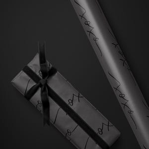 May include: A wrapped gift and a roll of gray wrapping paper with black cursive text that reads "xo". The gift is tied with a black ribbon. A white logo is in the upper right corner.