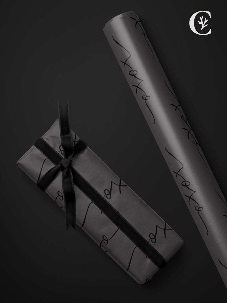May include: A wrapped gift and a roll of gray wrapping paper with black cursive text that reads "xo". The gift is tied with a black ribbon. A white logo is in the upper right corner.