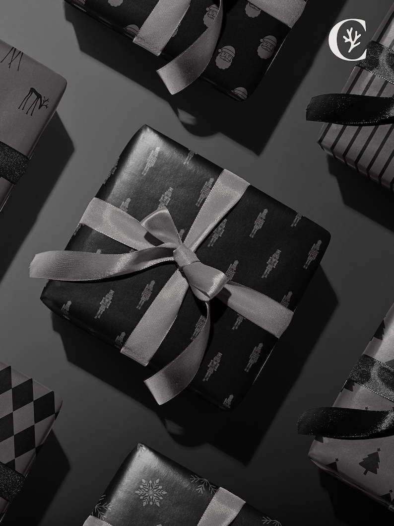 Peut inclure: Vue a&eacute;rienne de plusieurs cadeaux emball&eacute;s avec des rubans et des n&oelig;uds gris. Les cadeaux sont envelopp&eacute;s dans du papier noir avec divers motifs, notamment des flocons de neige, des rennes et le P&egrave;re No&euml;l. Le fond est gris fonc&eacute;.
