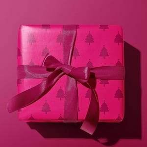 Pu&ograve; includere: Una confezione regalo magenta avvolta in carta con un motivo ripetuto di alberi di Natale rosa scuro. La scatola &egrave; legata con un nastro e un fiocco magenta abbinati, su uno sfondo magenta.