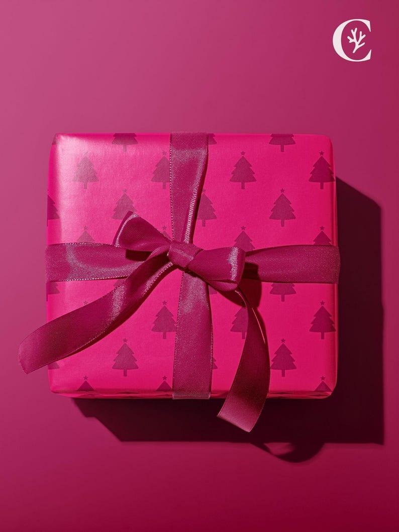 Pu&ograve; includere: Una confezione regalo magenta avvolta in carta con un motivo ripetuto di alberi di Natale rosa scuro. La scatola &egrave; legata con un nastro e un fiocco magenta abbinati, su uno sfondo magenta.