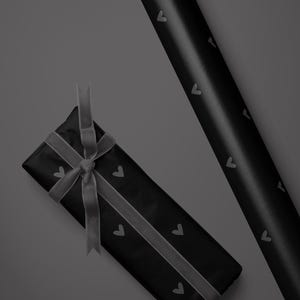May include: Black gift wrap with a repeating heart pattern, a wrapped gift with a gray ribbon, and a roll of matching wrapping paper. The gift is tied with a gray ribbon.