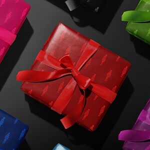 Op de afbeelding: Overzichtsfoto van ingepakte cadeaus in verschillende kleuren, waaronder rood, roze, blauw, groen en paars. Elk cadeau is verpakt in papier met patronen en vastgebonden met een bijpassend satijnen lint en strik. De cadeaus zijn gerangschikt op een zwarte ondergrond.