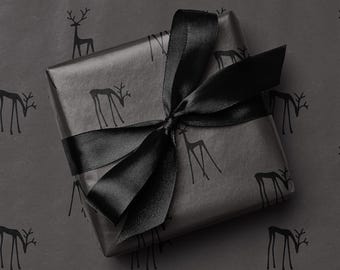 May include: A wrapped gift with black wrapping paper featuring a pattern of deer silhouettes. A black satin ribbon is tied in a bow on top. The gift is centered on a gray background with the same deer pattern.