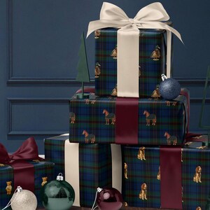 May include: Wrapped gifts with plaid patterned paper featuring ducks, horses, and dogs, tied with white and burgundy ribbons. Decorative Christmas ornaments in silver, green, and burgundy are arranged on a wooden surface, with a dark blue background.