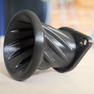 Op de afbeelding: Een zwarte, 3D-geprinte koffiedruppelaar met een uniek spiraalontwerp. De druppelaar heeft een brede opening aan de bovenkant en een platte basis met een gat voor montage. De binnenkant heeft schuine ribbels voor optimaal koffiezetten.