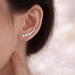 Op de afbeelding: Een zilveren oorcrawlers oorbellen met een reeks heldere, sprankelende edelstenen. De oorbel loopt langs het oor, waarbij de edelstenen in grootte afnemen. Het ontwerp is elegant en minimalistisch.