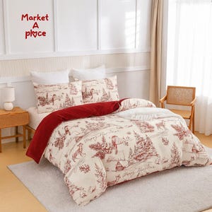 Op de afbeelding: Crèmekleurige dekbedovertrek en kussenset met een rood-wit toile de jouy ontwerp met winters scènes. Het dekbed heeft een rode fluwelen onderkant. De tekst "Happy New Year" is zichtbaar op het beddengoed. De tekst "Market A place" is zichtbaar.