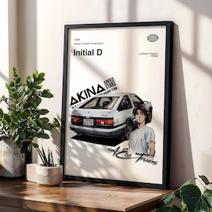 Op de afbeelding: Een ingelijste poster met de anime Initial D. De poster toont een witte auto, de tekst "AKINA SPEED STARS RACING TEAM" en een karakterillustratie. De poster zit in een zwarte lijst en staat op een houten oppervlak.