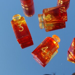 May include: Several amber-colored dice with gold numbering are scattered against a blue background. The dice are various shapes, including rectangular and multi-sided. The numbers 3, 4, 10, 15, 20, 60, and 90 are visible.