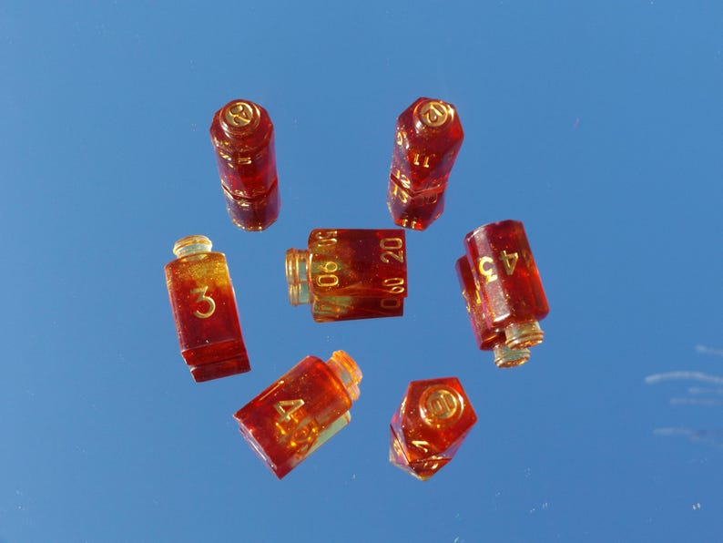 May include: A collection of small, transparent, amber-colored dice with gold-colored accents and numbers. The dice are arranged against a reflective, blue background. The numbers 3, 4, 45, 11, 10, 20, 60, and 90 are visible.