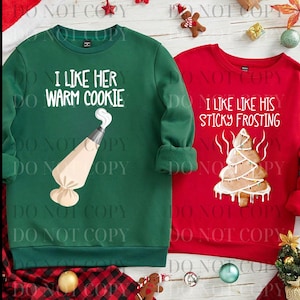 May include: Two Christmas-themed sweatshirts. One is green with the text "I LIKE HER WARM COOKIE" and a frosting bag graphic. The other is red with "I LIKE LIKE HIS STICKY FROSTING" and a gingerbread tree graphic.