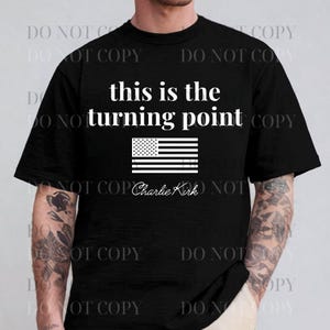 Puede incluir: Camiseta negra con el texto "this is the turning point" sobre un gráfico blanco de la bandera estadounidense. Debajo, la firma "Charlie Kirk". La camiseta es de cuello redondo.