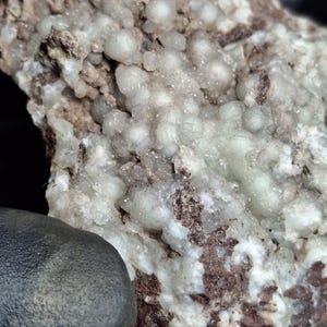 May include: Close-up of a mineral specimen featuring a light green, bubbly crystal formation on a matrix of white and brown rock. The texture is rough and uneven, with a mix of crystalline and earthy elements.