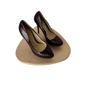 May include: A pair of burgundy-colored high-heeled pumps with a snakeskin pattern. The shoes are displayed on a light brown, wooden, triangular-shaped platform. The heels are approximately 4 inches tall.
