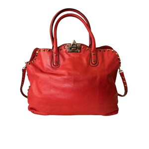 Peut inclure: Un sac &agrave; main en cuir rouge vif avec des clous dor&eacute;s. Le sac est dot&eacute; de deux poign&eacute;es sup&eacute;rieures et d'une bandouli&egrave;re amovible. La quincaillerie est dor&eacute;e et le sac a une forme classique et structur&eacute;e.