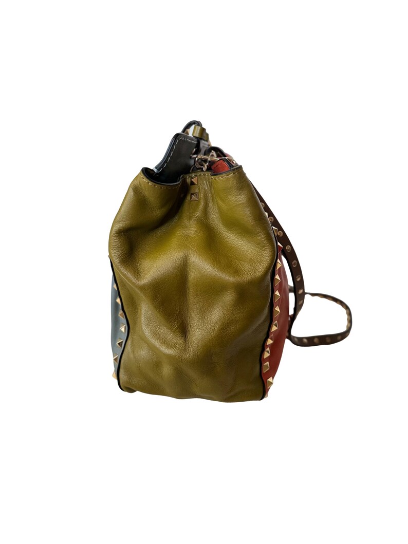 Puede incluir: Un bolso tipo cubo de cuero multicolor con cierre de cord&oacute;n. El bolso presenta paneles verde oliva, rojos y azules, acentuados con tachuelas doradas. El bolso tiene una correa de cuero marr&oacute;n.