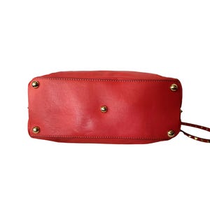 Peut inclure: Sac &agrave; main en cuir rouge avec des clous dor&eacute;s sur le fond. Le sac est de forme rectangulaire avec des coins arrondis. La base du sac est visible, avec des coutures et des &eacute;l&eacute;ments m&eacute;talliques.