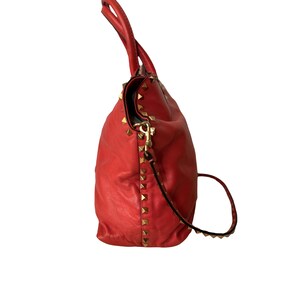 Peut inclure: Un sac &agrave; main en cuir rouge avec des clous dor&eacute;s. Le sac a une poign&eacute;e sup&eacute;rieure et une bandouli&egrave;re amovible. Le sac est fait d'un cuir souple et textur&eacute;.