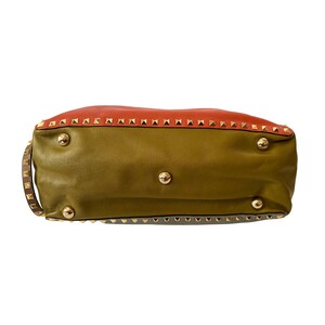 Puede incluir: Un bolso de mano de cuero con un dise&ntilde;o de bloques de color. La secci&oacute;n superior es naranja, la del medio es verde oliva y la inferior es verde azulado apagado. Se ven tachuelas y herrajes dorados.