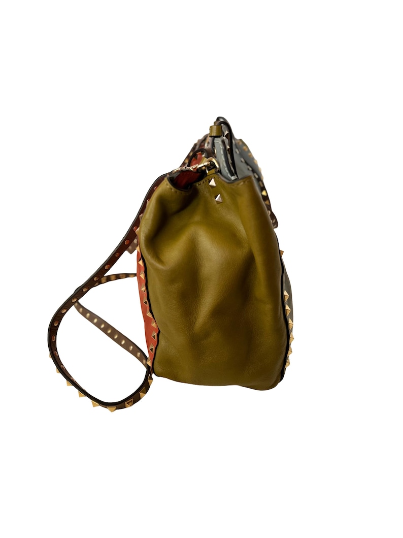 Puede incluir: Mochila de cuero verde oliva con correas marrones y tachuelas doradas. La mochila tiene un cierre de solapa y una secci&oacute;n estampada con detalles en rojo y gris. Las correas son ajustables.