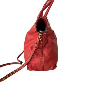 Peut inclure: Sac fourre-tout en cuir rouge avec des clous pyramidaux dor&eacute;s. Le sac est dot&eacute; d'une bandouli&egrave;re et de deux poign&eacute;es. L'int&eacute;rieur est noir. Le sac est en cuir souple et textur&eacute;.