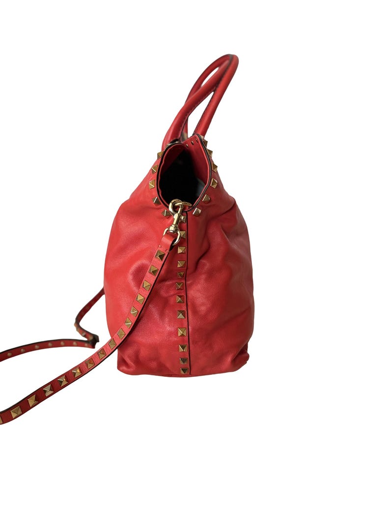 Peut inclure: Sac fourre-tout en cuir rouge avec des clous pyramidaux dor&eacute;s. Le sac est dot&eacute; d'une bandouli&egrave;re et de deux poign&eacute;es. L'int&eacute;rieur est noir. Le sac est en cuir souple et textur&eacute;.