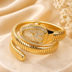 May include: A gold-tone wrap-around watch featuring a snake-shaped head with a white dial, gold hands, and Roman numeral markers. The bezel is encrusted with clear crystals, and the flexible, segmented band coils around the wrist in a spiral design.