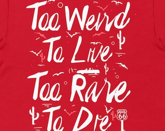 May include: A red t-shirt with the white text "Too Weird To Live, Too Rare To Die." The design includes illustrations of birds, cacti, and a Route 66 sign. The shirt is a crew neck and has short sleeves.