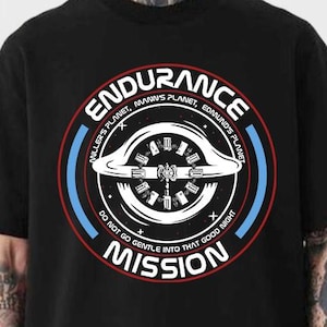 May include: Black t-shirt featuring a circular graphic with the word "ENDURANCE" in a red and white arc. The graphic includes the text "MILLER'S PLANET, MANN'S PLANET, EDMUND'S PLANET" and "DO NOT GO GENTLE INTO THAT GOOD NIGHT MISSION".
