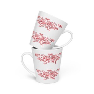 Op de afbeelding: Twee witte keramische latte mokken gestapeld, elk versierd met een herhalend rood drakenontwerp. De draak is afgebeeld op een gestileerde, sierlijke manier. De mokken hebben een gebogen handvat en een taps toelopende vorm.