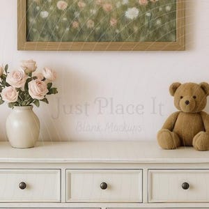 Puede incluir: Una escena de guardería con una cómoda de color claro con pomos negros, una impresión floral enmarcada, un jarrón con rosas rosas y un oso de peluche marrón. También son visibles una cuna y un cambiador, creando un ambiente suave.