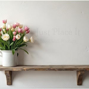 May include: A rustic wooden shelf with a white wall backdrop. A white metal bucket holds a bouquet of pink and white tulips and roses. The image has the text "Just Place It" in the background.