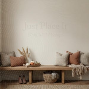 May include: A cozy interior scene featuring a wooden bench with decorative pillows in shades of beige and rust. A woven basket, pumpkins, and boots add to the autumnal theme. The wall has the text "Just Place It Blank Wall Mockups".