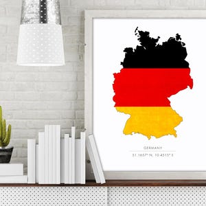 May include: A white framed print with a black and white outline of Germany with the German flag colors of black, red, and yellow. The text "GERMANY" and the coordinates "51.1657° N, 10.4515° E" are printed below the map.