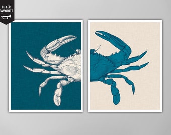 May include: Two framed art prints featuring detailed illustrations of crabs. One crab is depicted in white against a teal background, and the other is in teal against a beige background. The prints have a nautical theme.
