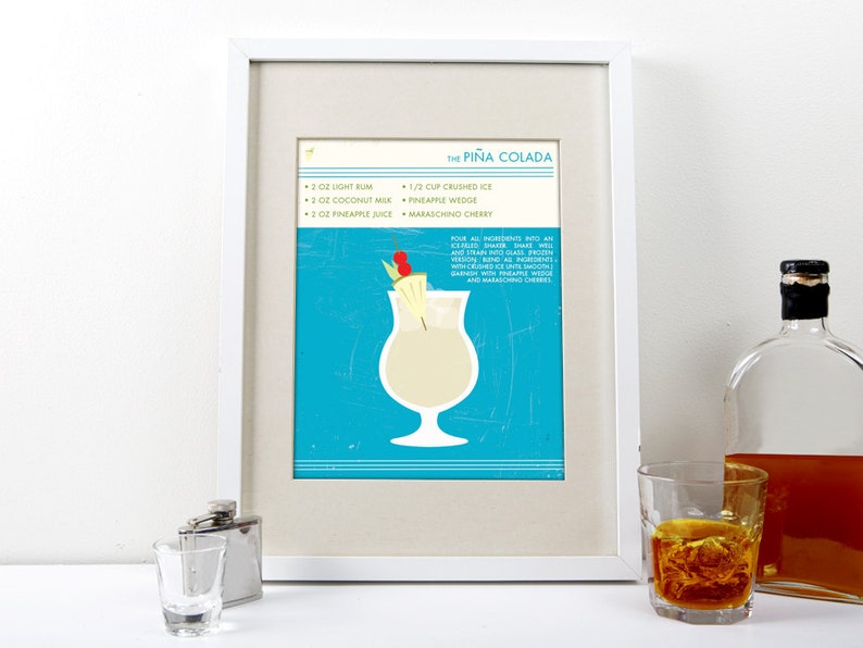Puede incluir: Una impresi&oacute;n enmarcada con un fondo azul y una copa de c&oacute;ctel blanca llena de una bebida cremosa. La impresi&oacute;n incluye la receta de una Pi&ntilde;a Colada, con ingredientes como ron blanco, leche de coco, jugo de pi&ntilde;a y hielo picado. El texto tambi&eacute;n incluye instrucciones para agitar todos los ingredientes con hielo y colar en un vaso.