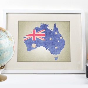 May include: A framed print of a map of Australia with the Australian flag superimposed on it. The map is printed on a textured paper with a vintage look. The frame is white with a white mat.