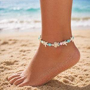 May include: Ankle bracelet with white starfish, turquoise and pink beads, and a turtle charm. The jewelry is worn on an ankle on a sandy beach with the ocean in the background.
