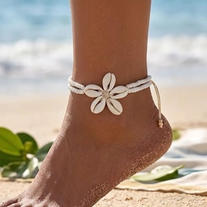 May include: An anklet featuring a central flower motif crafted from five white cowrie shells. The band consists of two rows of small white beads, with a thin cord extending from the side, finished with a single small bead at the end of the string.