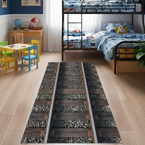 May include: A rectangular rug with a railroad track design. The rug features parallel silver tracks, wooden ties, and gray gravel. The rug is placed on a light-colored wooden floor in a child's bedroom, with a bunk bed in the background.