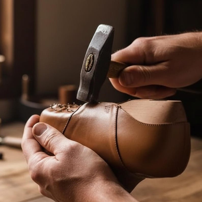 Puede incluir: Una parte superior de zapato de cuero color canela montada sobre una horma de madera, trabajada con un martillo de metal. El zapato presenta costuras visibles a lo largo de las uniones y varios clavos met&aacute;licos peque&ntilde;os en el cuero.