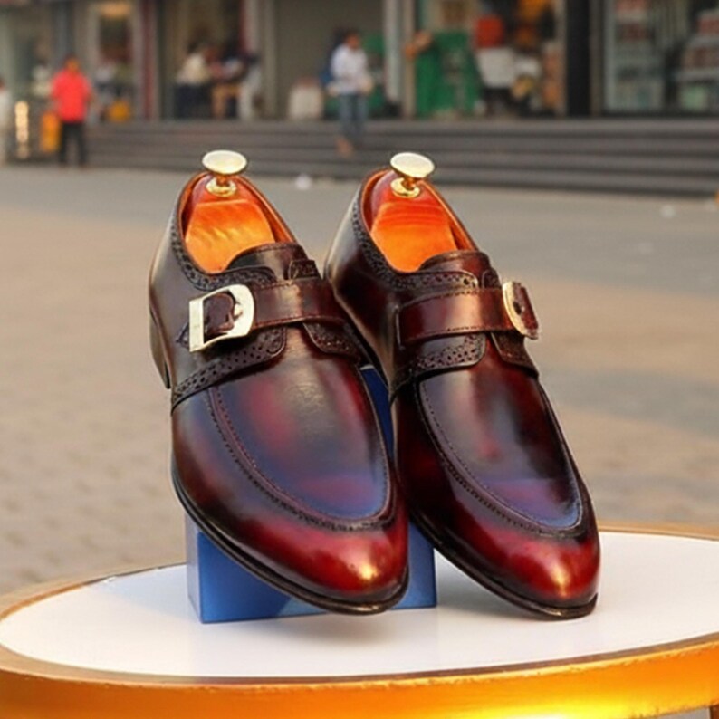 Pode incluir: Um par de sapatos de couro bord&ocirc; com fecho de fivela. Os sapatos t&ecirc;m um acabamento polido e um design decorativo nas bordas. O interior &eacute; de cor laranja brilhante.