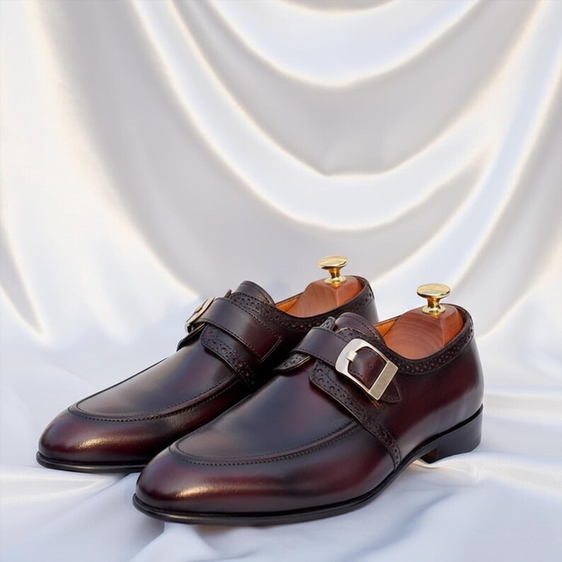 Pode incluir: Um par de sapatos de couro bord&ocirc; com fivela de tira. Os sapatos t&ecirc;m um design cl&aacute;ssico com bico fino e costuras decorativas. As formas est&atilde;o dentro dos sapatos.