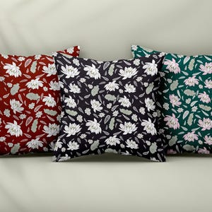 May include: Three square throw pillows with floral patterns. One pillow is burgundy with white flowers, another is black with white flowers, and the third is dark green with pink flowers. The pillows are arranged side by side.